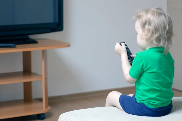 A child with a remote control in his hand turns on the TV to watch cartoons — Stock Photo, Image
