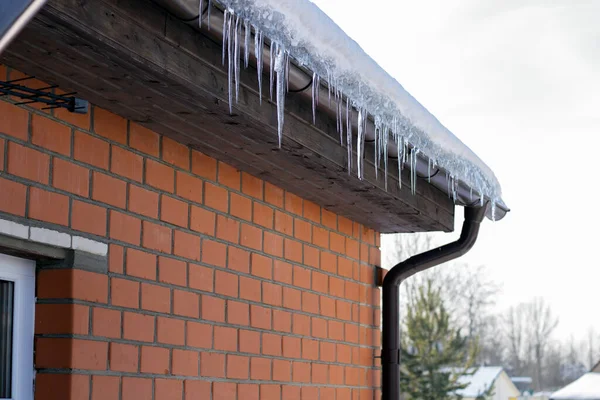 IJspegels op de dakrand van een stenen huis, temperatuurdaling. Het smeltwater stroomt geleidelijk naar beneden — Stockfoto