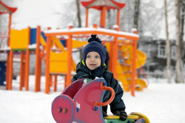 Kış tulumu giymiş bir çocuk oyun bahçesinde dururken gülümsüyor. — Stok fotoğraf