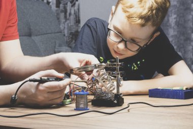 El ve lehim. Elinde lehim makinesi olan bir adam ve süreci izleyen bir çocuk. Seçici odak, mat etkisi