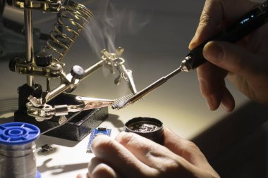 Lehim demiri dumanı ve modern termodinamik lehimleme demiri tutan bir el. Koyu tonlar, seçici odak