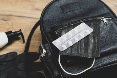 Womens backpack and a medical mask with medicines in an open pocket next to medical gloves.