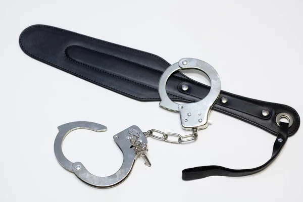 Kelepçeler ve beyaz arka planda deri bir kürek yetişkin seks oyuncakları.