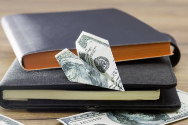 Kağıt paralarla dolu bir not defterine kağıt dolarlık uçak. İş ve finans. Not defterinde para var. İş ve finans