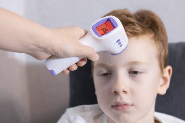 El modern elektronik kızılötesi termometre kullanıyor, çocukların vücut ısısı ölçülüyor. COVID-19.