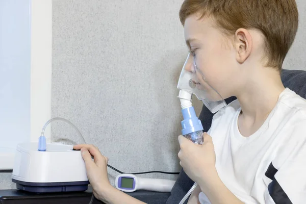 Medische inhalatietherapie. De jongen ademt met het gezichtsmasker van een moderne jet vernevelaar. Rechtenvrije Stockafbeeldingen