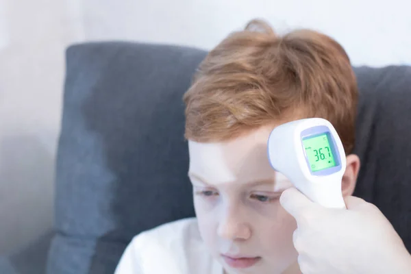 Een hand houdt een contactloze thermometer vast met een infrarood pistool en meet de temperatuur van een kind met rood haar. Rechtenvrije Stockfoto's