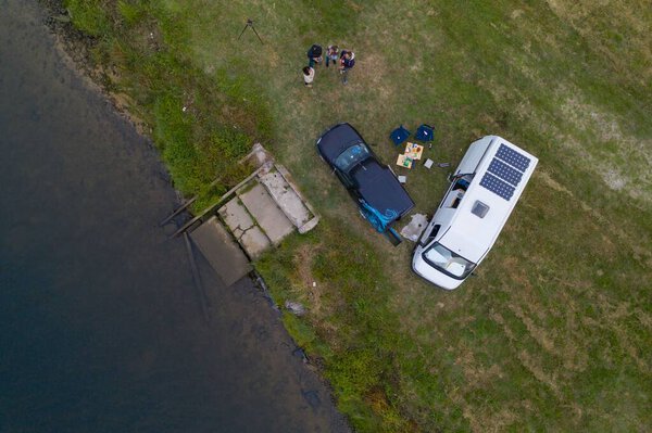 Camper van motorhome with solar panels drone aerial view of two couples living van life near a river and grass in Portugal at sunset