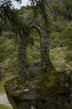 Ancient ruin stone structure building covered with moss near Sao Pedro chapel with trees and boulder landscape in Monsanto, Portugal