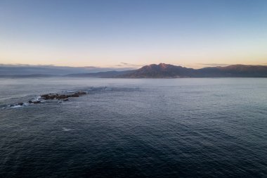 Atlantik Okyanusu 'ndaki dağların insansız hava aracı manzarası Galiza, İspanya' da Caldebarcos 'ta gün batımında dalgalarla birlikte.
