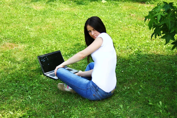 Hermosa joven estudiante usando el ordenador portátil en la hierba — Foto de Stock