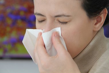 Grip, soğuk algınlığı, ateşi ve öksürüğü olan hasta bir kadın evdeki kanepede oturuyor. Burun sümküren ve mendille hapşıran hasta..