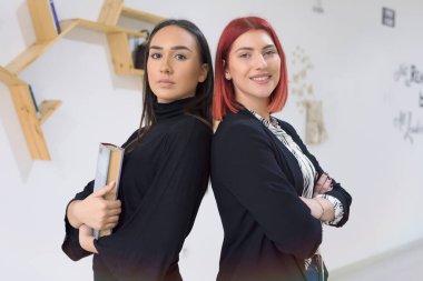 Üniversitenin içinde poz veren gülümseyen bayan öğrenciler