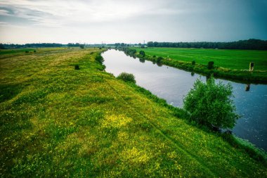 Vecht nehrinin insansız hava aracı görüntüsü, yeşil çimenler, mavi su, yüksek voltaj direkleri olan şehir. Vechtdal, Hollanda Dalfsen.