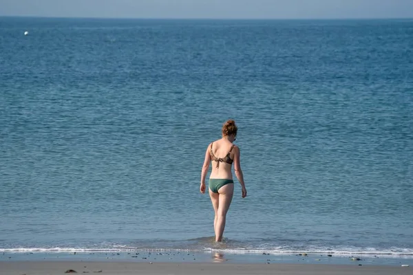 Νεαρή γυναίκα με καστανά μαλλιά στέκεται στη θάλασσα. Φοράει αντηλιακό. Mall κύματα γύρω από τα πόδια της. Μόνος στον κόσμο, διακοπές, ελευθερία — Φωτογραφία Αρχείου