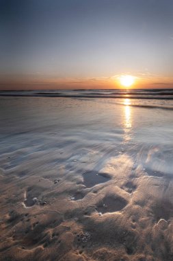 Uzun pozlama, turuncu gün batımlı deniz, kumdaki deniz kabukları. Soyut görünüm, arkaplan, kart, tebrik kartı, yas kartı.
