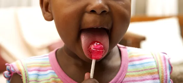 Svart tjej suger lollipop — Stockfoto