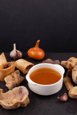 Siyah taş masadaki beyaz kasede ev yapımı haşlanmış et kemiği çorbası. Koyu arkaplan, seçici odaklanma, kopyalama alanı. Altın et bulyonu. Kemikler kolajen içerir.