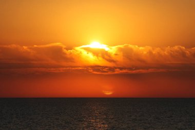 Denizde gün batımı. Güneş ufukta batıyor, bulutlar kırmızı ve turuncu oluyor..