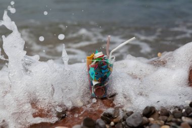 Plastik bir bardakta denizden gelen plastik çöpler. Kavram - tehlikeli deniz kokteyli, ev çöpleriyle çevre kirliliği.