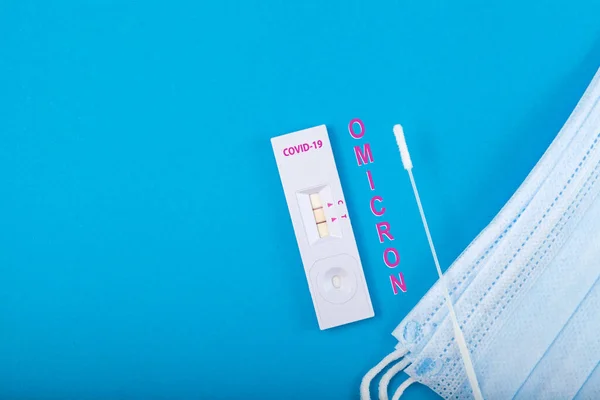 Omicron, yeni Coronavirus versiyonu. Hastalardaki koronavirüsü tanımlamak için hızlı antijen testi. Tıbbi maskeye bak. Mavi arkaplan, boşluğu kopyala.