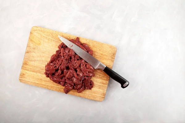 Beef liver and kitchen knife on wooden chopping board, top view. Raw offal, cut into pieces.
