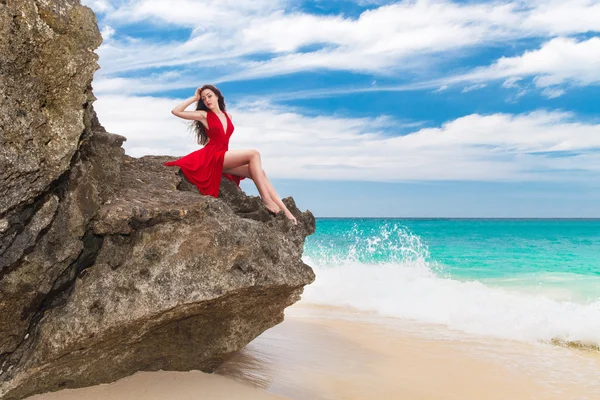 年轻美丽的独自坐在岩石的红色连衣裙女人 — 图库照片