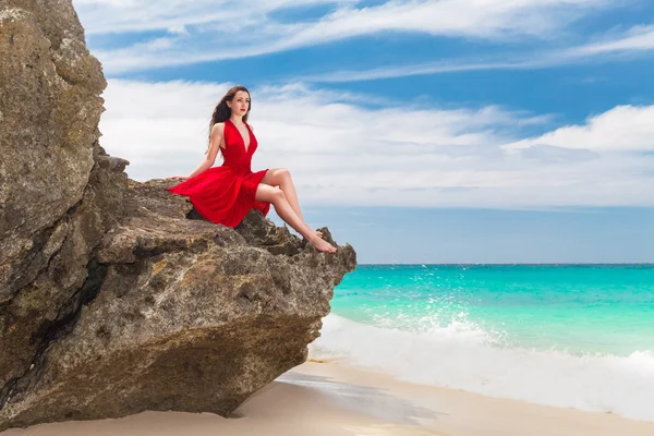 Νεαρή όμορφη γυναίκα μόνο σε κόκκινο φόρεμα να κάθεται πάνω στο βράχο στο — Φωτογραφία Αρχείου