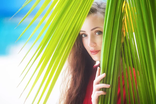 Uma menina bonita olhando através de folhas de palma, vac tropical — Fotografia de Stock