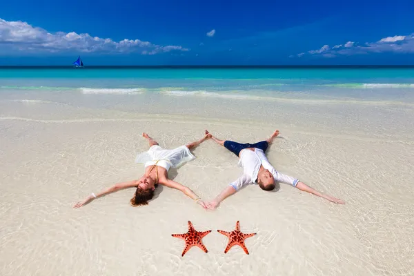 Novia y novio acostado en la orilla de la playa con dos estrellas de mar — Foto de Stock