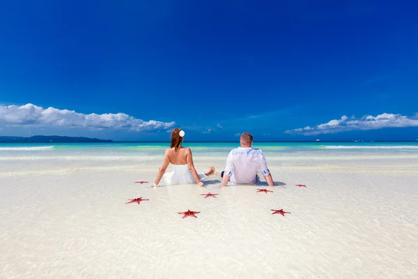 Braut und Bräutigam springen mit roten Seesternen am tropischen Strand — Stockfoto