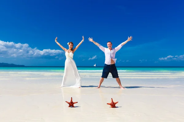 Bride and Groom standing on tropical beach shore with two red st — Stock Photo, Image