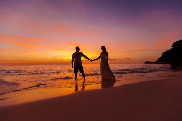 Bride and groom on a tropical beach with the sunset in the backg — Stock Photo, Image
