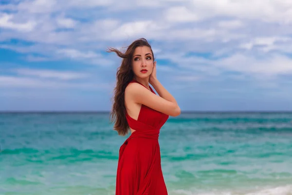 Krásná žena v červených šatech, stojící na pobřeží moře — Stock fotografie