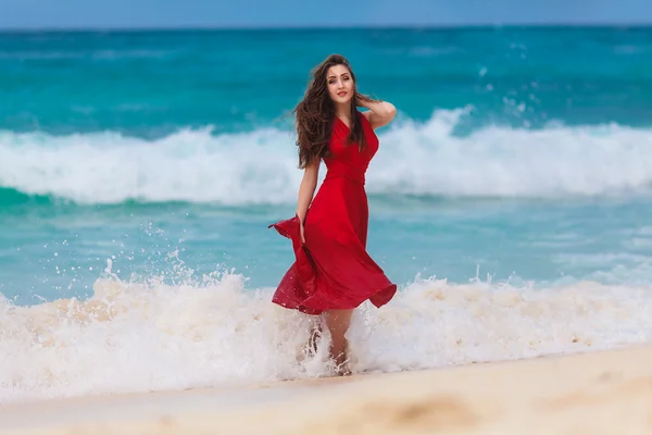 Krásná žena v červených šatech na pobřeží tropické moře — Stock fotografie
