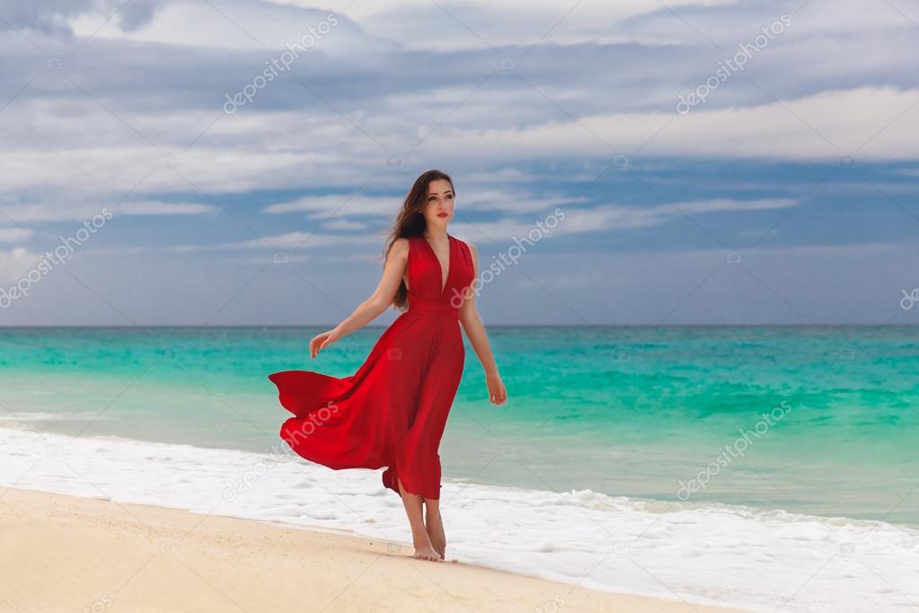 Beautiful woman in a red dress  standing on the sea coast