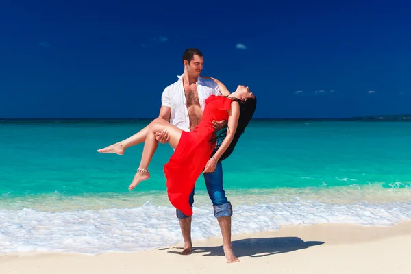 Young handsome man holds a beautiful brunette in a red dress on — Stock Photo, Image