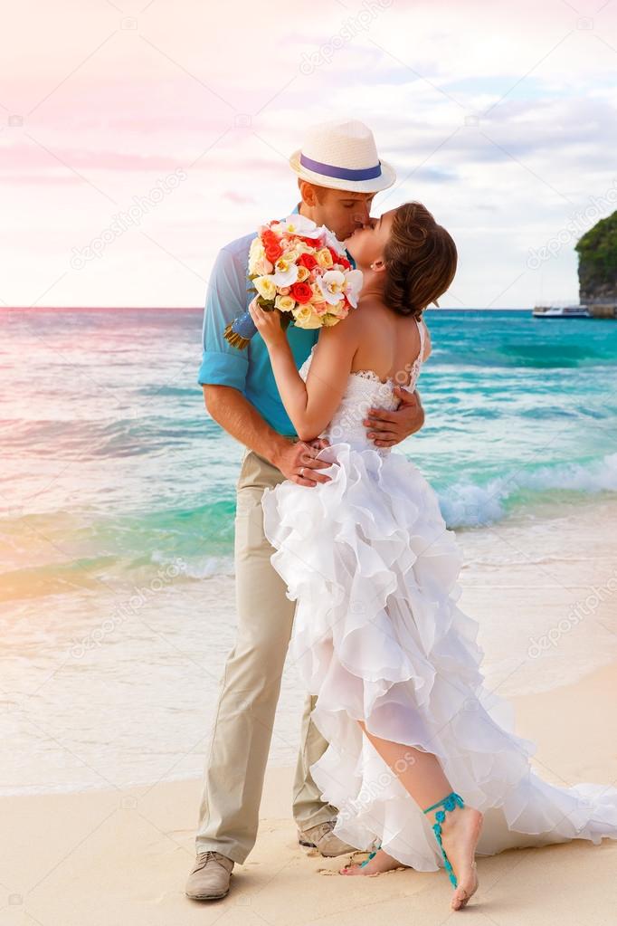 Wedding. Bbride and groom kissing on the tropical coast at sunse