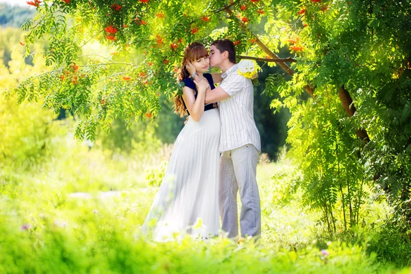 Glückliches und junges schwangeres Paar, das sich im Park umarmt. Sommerurlaub — Stockfoto