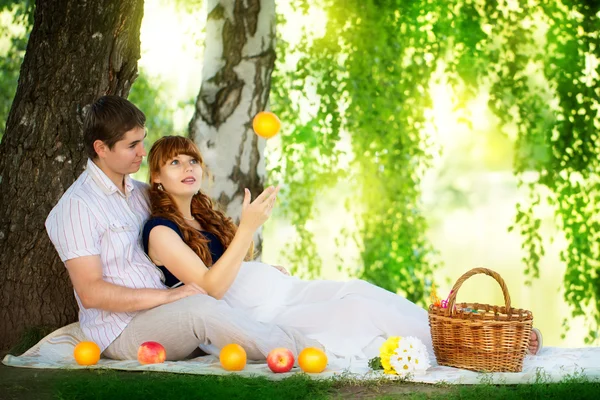 Feliz e jovem casal grávida abraçando na natureza desfrutando de summe — Fotografia de Stock