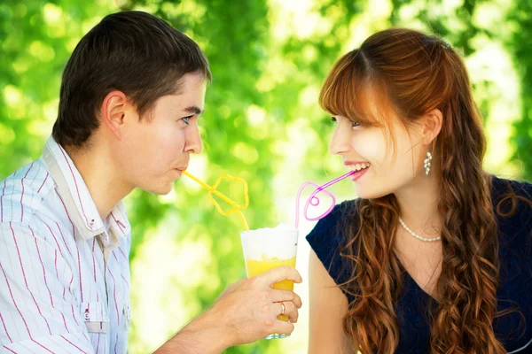 Молодая пара пьет сок из одного стакана с краской — стоковое фото