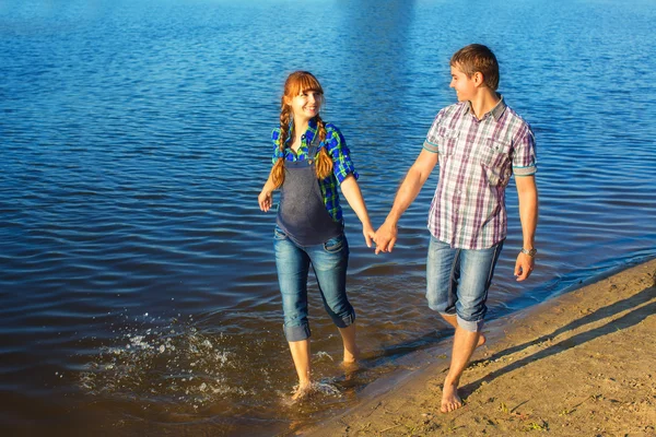 Glad och unga gravida par att ha kul på stranden. sommar — Stockfoto