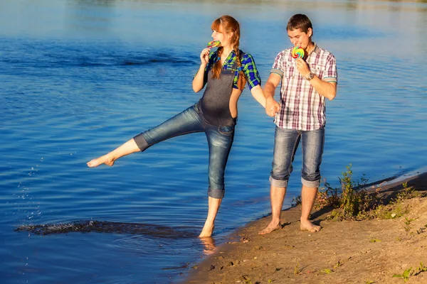 Glad och unga gravida par att ha kul på stranden. sommar — Stockfoto