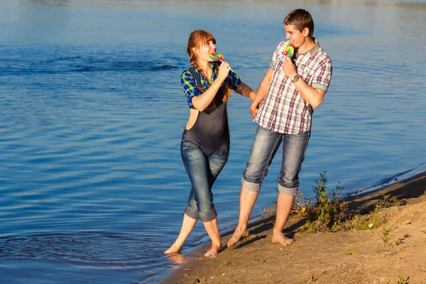 Glad och unga gravida par att ha kul på stranden. sommar — Stockfoto