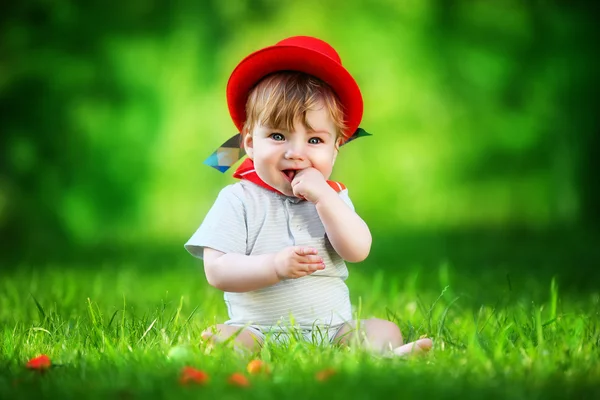 Happy little baby in red hat having fun in the park on solar gla — Stock Photo, Image