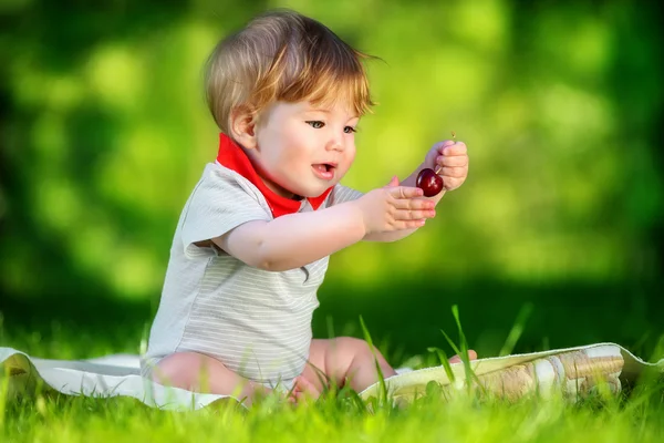 Gelukkig baby hebben plezier in het park op een zonnige weide met kersen. — Stockfoto