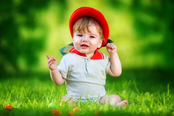 Happy little baby in red hat having fun in the park on solar gla — Stock Photo, Image