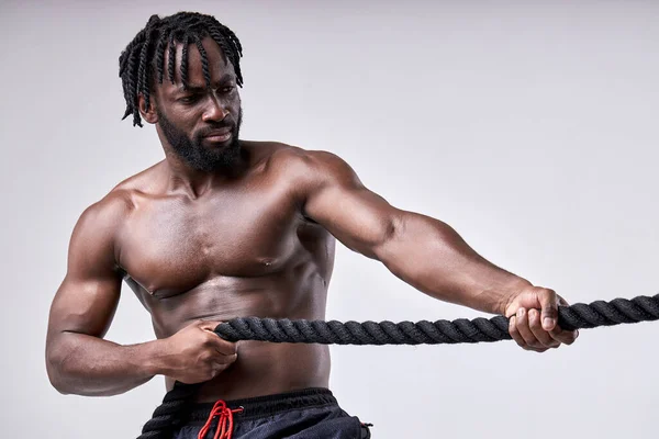 Atleta africano serio tirando de la cuerda cruzada en forma aislada sobre fondo blanco — Foto de Stock