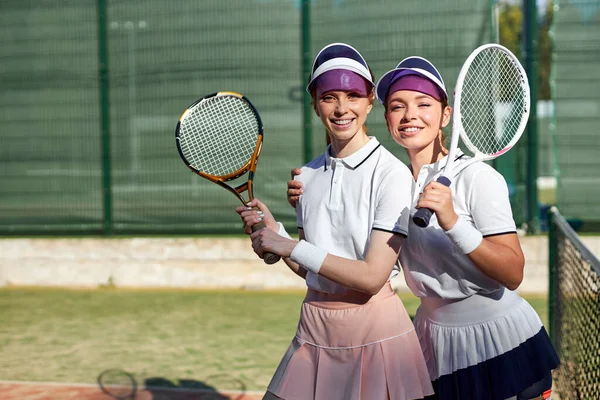Δύο ενθουσιασμένες λευκές γυναίκες στο γήπεδο. Γυναίκες με αθλητική στολή με ρακέτα του τένις — Φωτογραφία Αρχείου