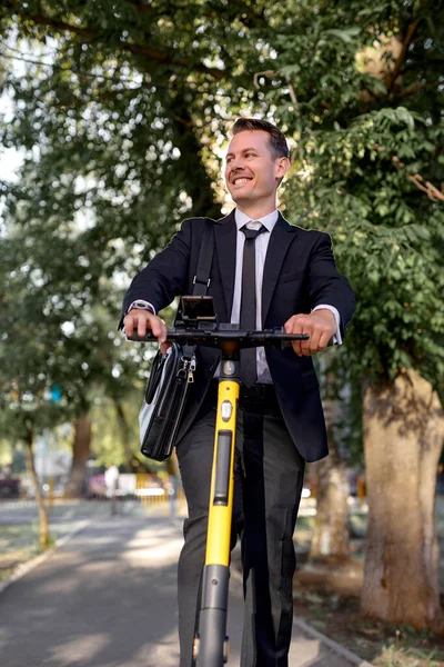 Young handsome business man in suit riding electric scooter goes to the office